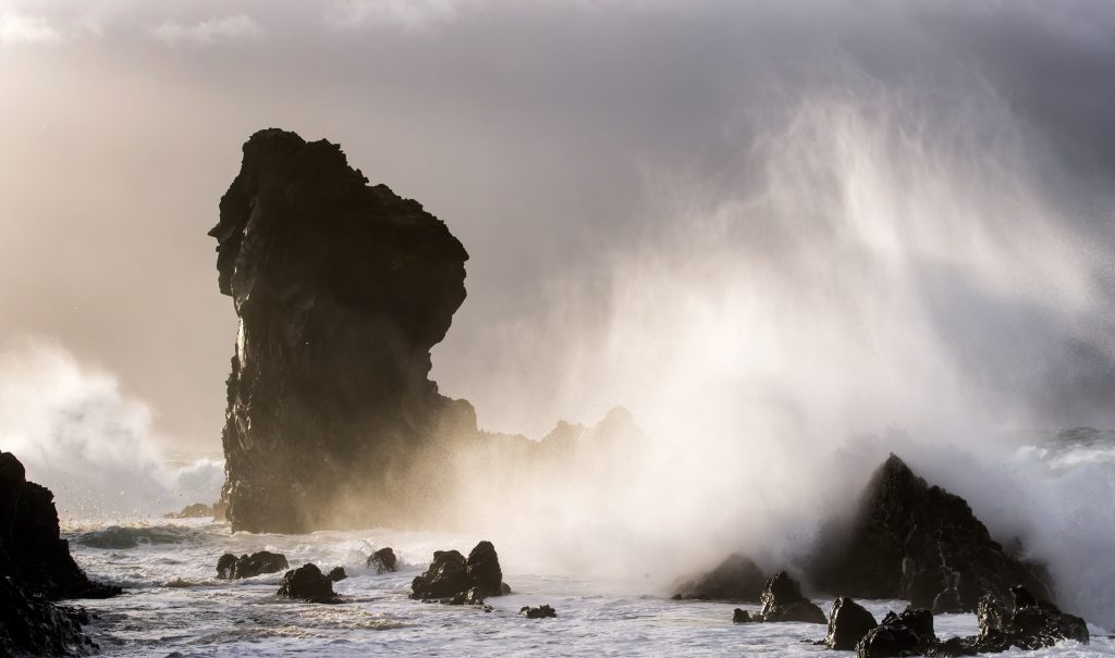 Crashing waves cover a sea stack in Iceland.